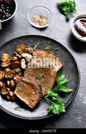 Carne di manzo con funghi e salsa di mirtilli sulla pietra scuro dello sfondo. Saporiti stufati di carne con funghi e salsa dolce. Foto Stock