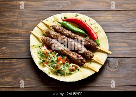 Bagno turco Adana Kebab con verdure fresche su flatbread su un tavolo di legno. Gustosi piatti in stile arabo Foto Stock