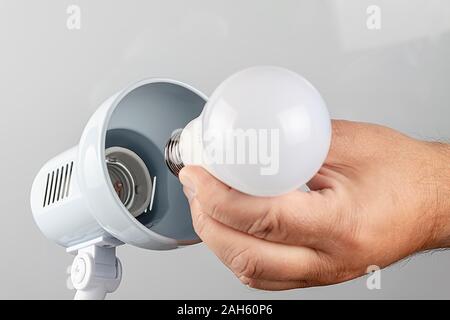 La mano tiene la lampadina per ruotarla nella lampada. Foto Stock