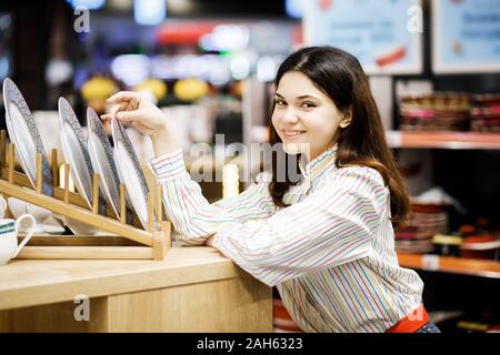 Piuttosto giovane bruna ragazza sceglie stoviglie al supermercato. Foto Stock