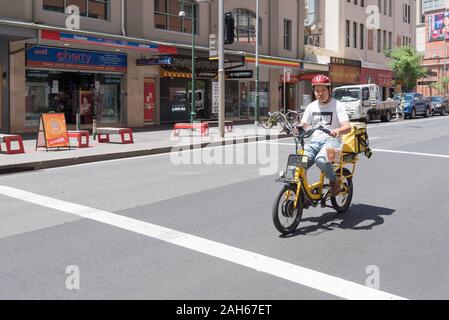 Un uomo cinese cavalca un servosterzo pushbike in Cina il distretto della città di Sydney CBD erogazione di fast food e drink per Easi consegne alimentari Foto Stock