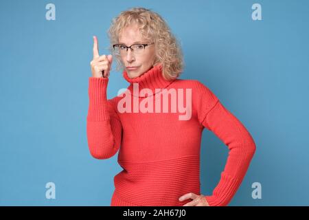 Grave donna in bicchieri puntare il dito indice fino dare consigli. Foto Stock