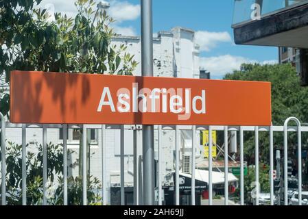 Un brillante arancio e bianco scritte segno annuncia Ashfield Stazione Ferroviaria per chiamate in arrivo e per scendere i passeggeri del treno Foto Stock