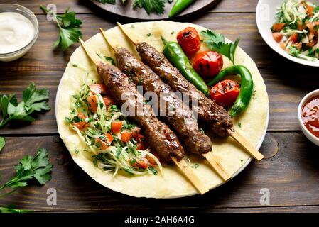 Bagno turco Adana Kebab con verdure fresche su flatbread su un tavolo di legno. Gustosi piatti in stile arabo Foto Stock