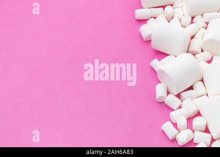 Un gruppo di piccoli e grandi marshmallows che copre il lato destro di un sfondo rosa Foto Stock