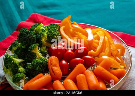 Un piatto di vetro di materie verdure consiste di cime di broccoli, baby carote, pomodori uva e fette di giallo i peperoni. Foto Stock