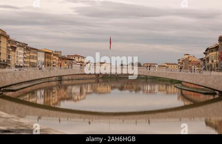 Un inizio serata foto del piatto e tranquillo fiume Arno passando attraverso il centro di Pisa con colorati edifici vecchi e ponte riflessa nel fiume. Foto Stock