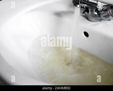 Qualità scarsa alimentazione idrica, scorre dal rubinetto domestico nel lavandino del bagno. Malsana sporca, colore marrone. Foto Stock