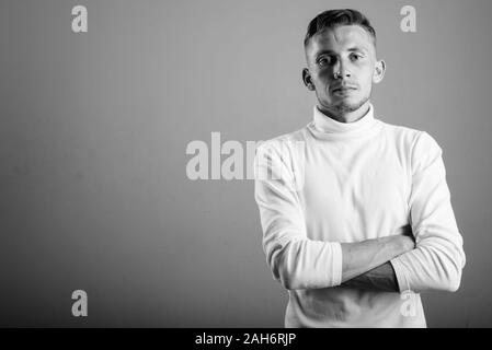 Giovane uomo che indossa bianco maglione turtleneck contro uno sfondo grigio Foto Stock