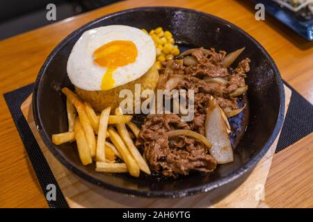 Sizzling di filetto di manzo riso servito con patate fritte e uova Foto Stock