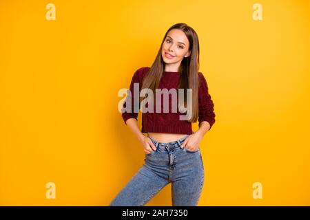 Ritratto di carino giovane mettendo le mani in tasca dei jeans denim, indossando maroon pullover isolate su sfondo giallo Foto Stock