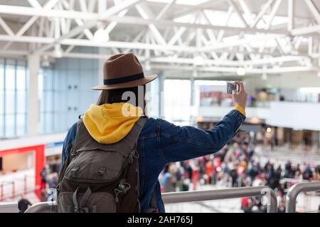 Vacanza Selfie. Bella giovane donna nel cappello e camicia di jeans tenendo selfie durante l'attesa per l'imbarco in aeroporto. Foto Stock