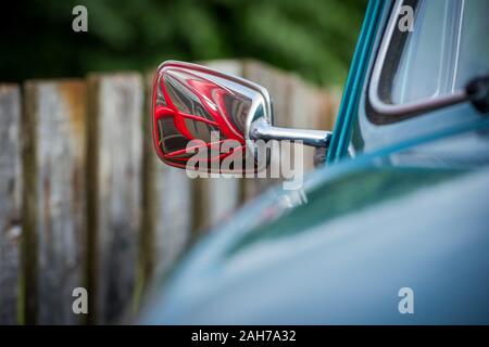 Primo piano dello specchietto retrovisore di una vecchia luce auto blu che riflette una tradizionale cabina telefonica rossa britannica contro uno sfondo bokeh Foto Stock