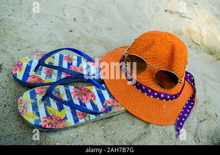 Orange hat, flip-flop e occhiali da sole sulla bianca spiaggia di sabbia Foto Stock