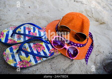 Orange hat, flip-flop e occhiali da sole sulla bianca spiaggia di sabbia Foto Stock