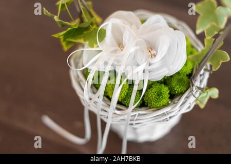 Due anelli dorati di nozze sono tenuti su un cuscino bianco all'interno di un cesto di vimini decorato con edera Foto Stock