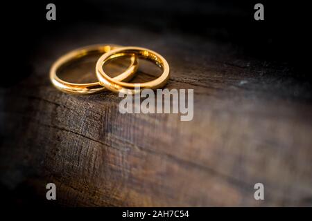 Primo piano di due anelli di nozze dorati che giacciono sul bordo di un antico tavolo di legno intemperie Foto Stock