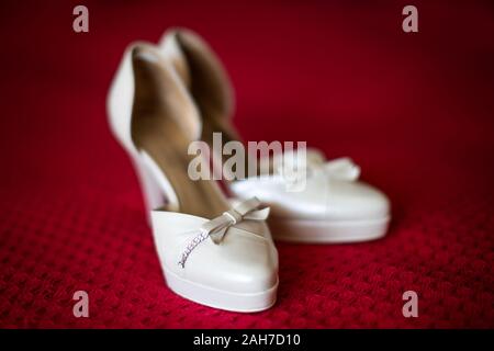 Primo piano di un paio di bianco elegante high-heels matrimonio scarpe giacenti su lino scarlatto Foto Stock