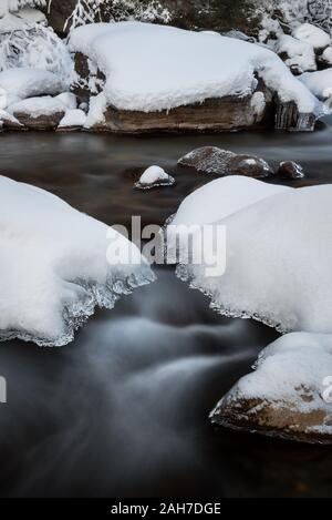 Da vicino si può ammirare il paesaggio invernale, con un getto d'acqua fredda che scorre tra rocce innevate e nelle rapide Foto Stock