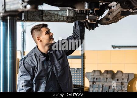 Giovanissimo meccanico ispezione sollevate auto in officina Foto Stock