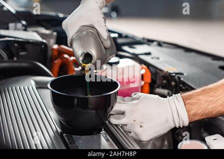 Vista ritagliata di meccanico versando olio per auto a motore Foto Stock