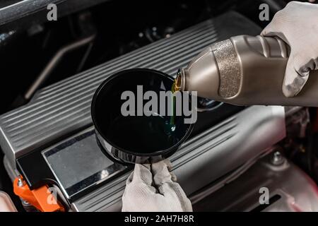 Vista ritagliata di meccanico versando l'olio di lubrificazione in imbuto Foto Stock