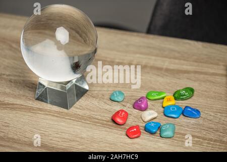 Sfera di cristallo e le pietre colorate con segni zodiacali sul tavolo di legno Foto Stock