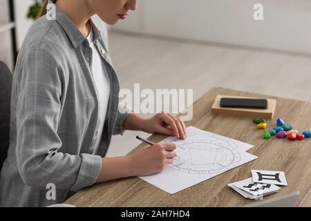 Vista ritagliata della donna disegno Natal grafico dalle carte con segni zodiacali sul tavolo Foto Stock