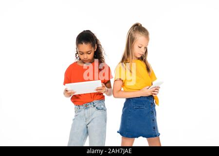 Due attenti amici multiculturale utilizza lo smartphone e tablet digitale isolato su bianco Foto Stock