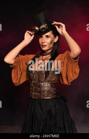 Attraente steampunk donna con il trucco di mettere su top hat sul nero nel fumo di colore rosa Foto Stock