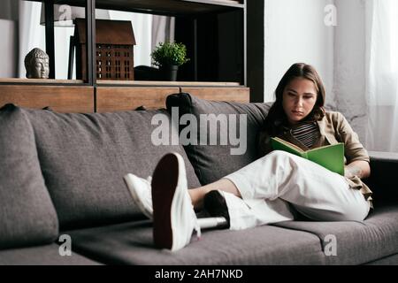 Messa a fuoco selettiva di donna con gamba protesico leggendo un libro sul divano nel soggiorno Foto Stock