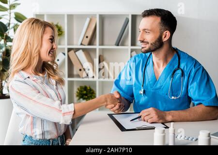 Donna felice stringono le mani con barbuto medico in clinica Foto Stock