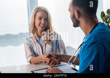 Messa a fuoco selettiva di allegra donna stringono le mani con barbuto medico in clinica Foto Stock