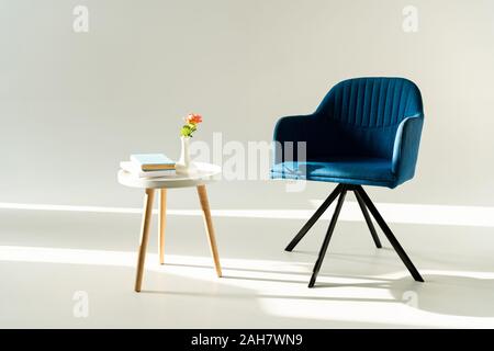 Blu poltrona moderna e tavolo da caffè con fiore in vaso e libri su sfondo grigio Foto Stock