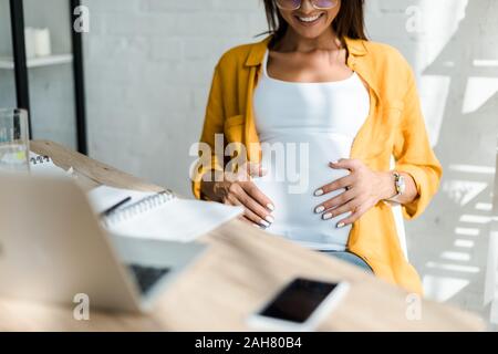 Vista ritagliata della gravidanza sorridente freelancer in seduta home office Foto Stock