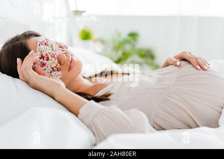 Donna incinta giacente nella maschera di dormire nel letto Foto Stock