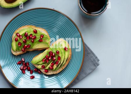 Sandwich di Avocado sul pane fresco con fette di avocado e i semi di melograno su grigio Sfondo di legno. Vista dall'alto. Mangiare sano concetto. Copia spac Foto Stock