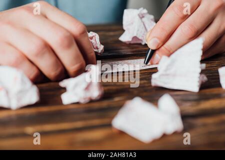 Vista parziale del giocatore i numeri di marcatura nel biglietto della lotteria vicino accartocciata lotteria carte sul tavolo di legno Foto Stock