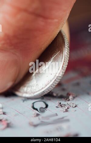 Vista ravvicinata della moneta d'argento nella mano del giocatore di graffiare la scheda della lotteria Foto Stock