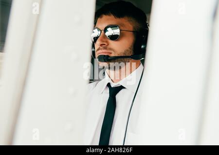 Grave pilota in occhiali da sole e la cuffia che guarda lontano Foto Stock