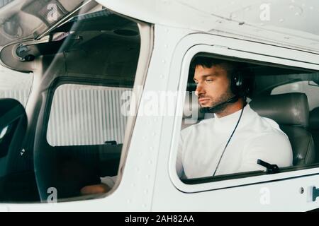 Focalizzato pilota barbuto in cuffia seduto in aereo Foto Stock