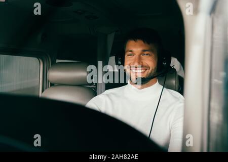 Sorridente bello barbuto pilota in cuffia in piano Foto Stock