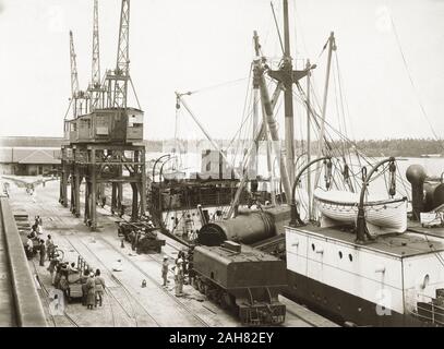 Il Kenya, una locomotiva a vapore e dei bandi di gara nel processo di essere scaricati dalla nave da carico SS Harmonides a Kilindini Harbour. Gli operai sono in piedi vicino a. Parte di una serie che mostra la locomotiva di scarico, [1920]. 1999/135/1/1/2. Foto Stock