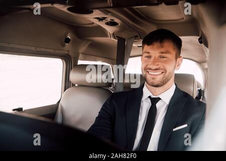 Sorridente pilota barbuto in abbigliamento formale seduto in aereo Foto Stock