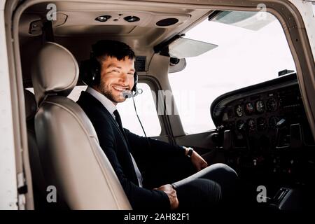 Sorridente pilota barbuto in abbigliamento formale seduto in aereo Foto Stock