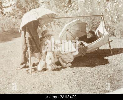 India, due giovani donne europee lounge in un amaca in giardino, probabilmente in Simla, ombreggiatura stessi dal sole con ombrelloni come rilassarsi e leggere libri. Questa fotografia è una copia di un'altra immagine dello stesso album, dove le donne sono didascalie come 'K' e Peggy, 1920. 2001/243/1/1/2/100. Foto Stock