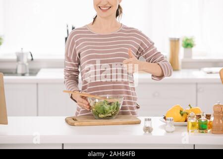 Vista ritagliata della donna sorridente che mostra un pollice alzato in piedi vicino a coppa con fresca insalata di verdure Foto Stock