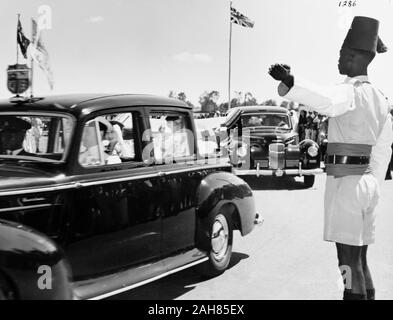 Il Kenya, la Principessa Elisabetta e il Duca di Edimburgo in auto da Eastleigh Airport in una macchina che porta le insegne regali. Dietro questa macchina aziona un'altra auto anche il cuscinetto del Royal Crest. Un africano funzionario di polizia punti nella direzione di marcia, febbraio 1952. 2001/090/1/4/1/16. Foto Stock