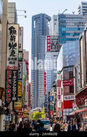La massiccia torreggianti Governo Metropolitano di Tokyo edificio, o a Tokyo Tocho, visto da una stretta occupato affollata strada commerciale di Shinjuku. Foto Stock