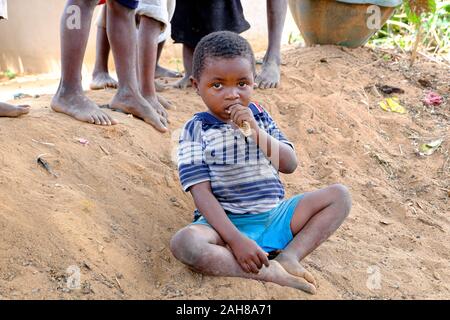 Bambino africano con la maglietta blu e pantaloncini blu seduta sul pavimento Foto Stock